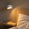 Witte oplaadbare magnetische wandlamp naast een bed met warm gericht licht